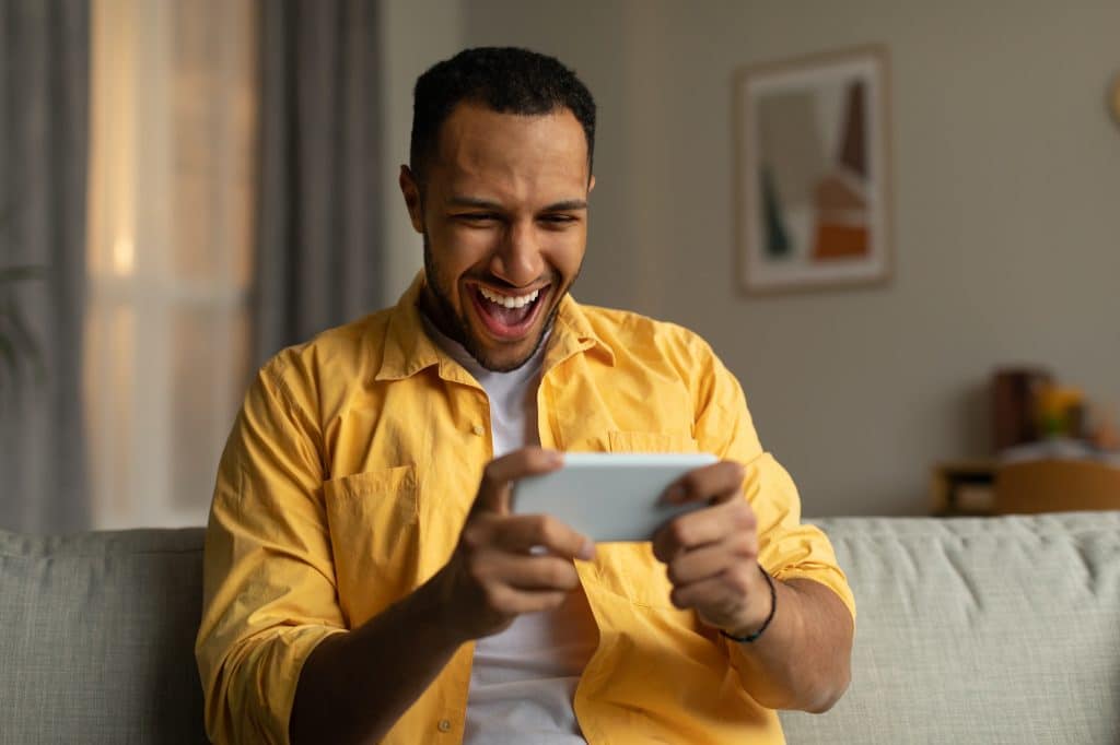 Overjoyed young black man with smartphone feeling excited over winning lottery or casino bet online