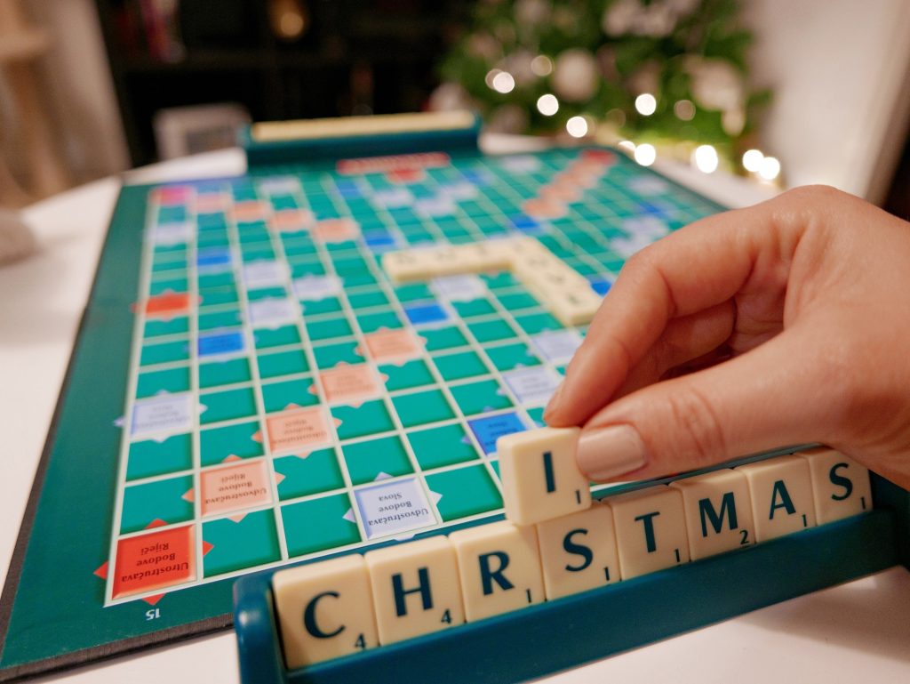 Scrabble board game on table. Hand holding letter tiles and putting together word christmas.