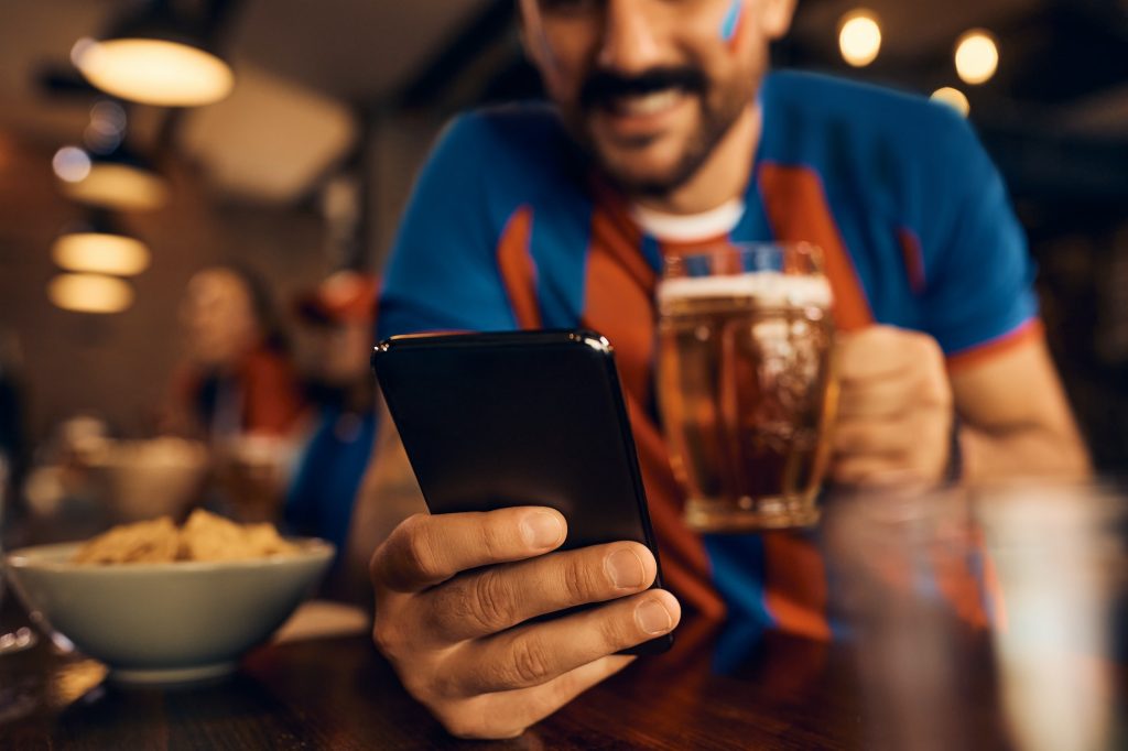 Close up of sports fan using cell phone in a bar.