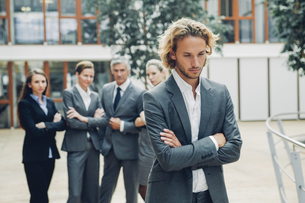 Businessman with crossed arms, excluded from group of business people